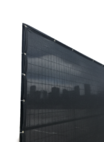 A black privacy mesh screen securely installed on a temporary wire fence panel using zip ties, partially obscuring a city skyline to demonstrate its effective visual barrier for job sites.