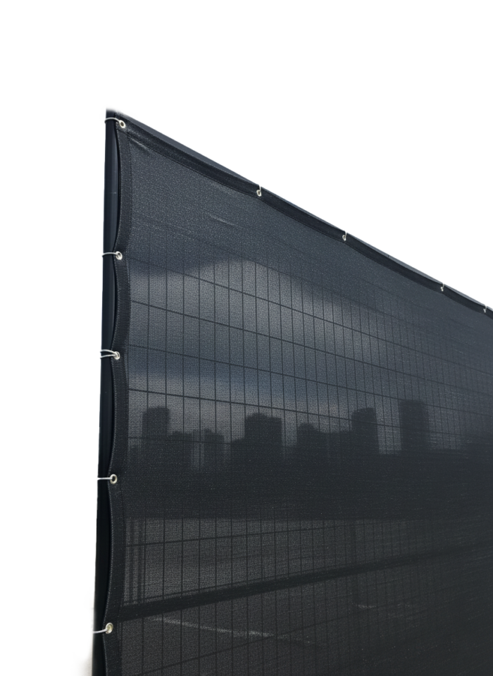 A black privacy mesh screen securely installed on a temporary wire fence panel using zip ties, partially obscuring a city skyline to demonstrate its effective visual barrier for job sites.