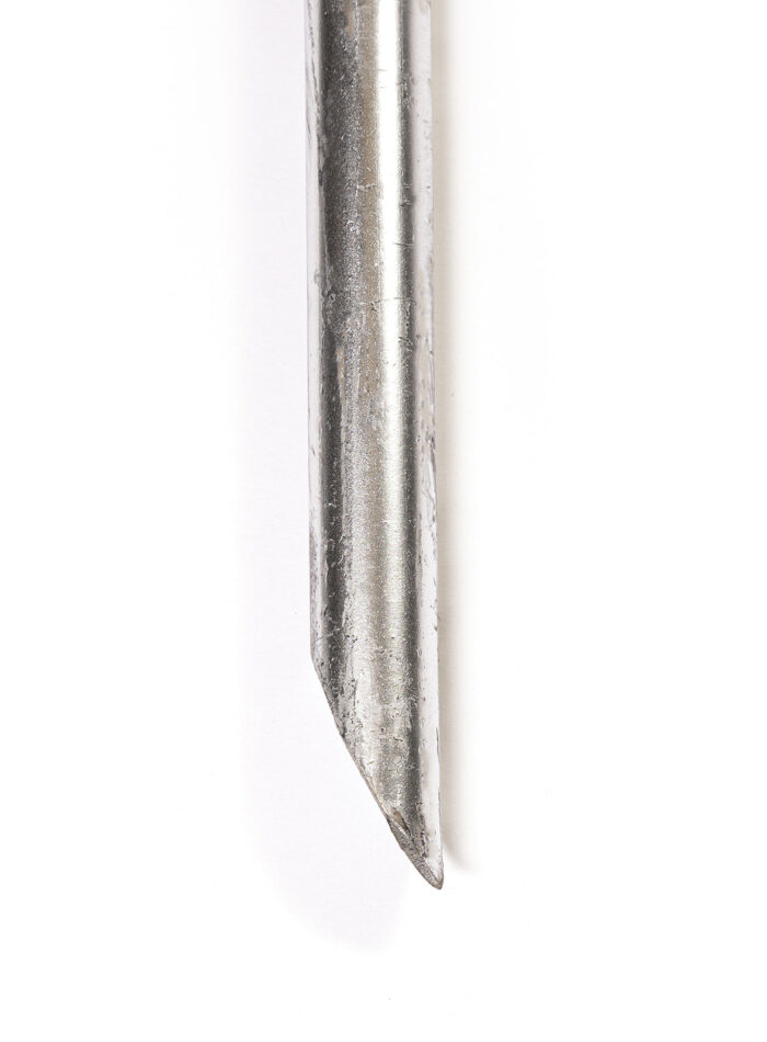 A detailed close-up of the bottom end of a galvanized steel ground pin, showing its angled chisel-cut tip engineered for easier driving into compacted soil or asphalt.