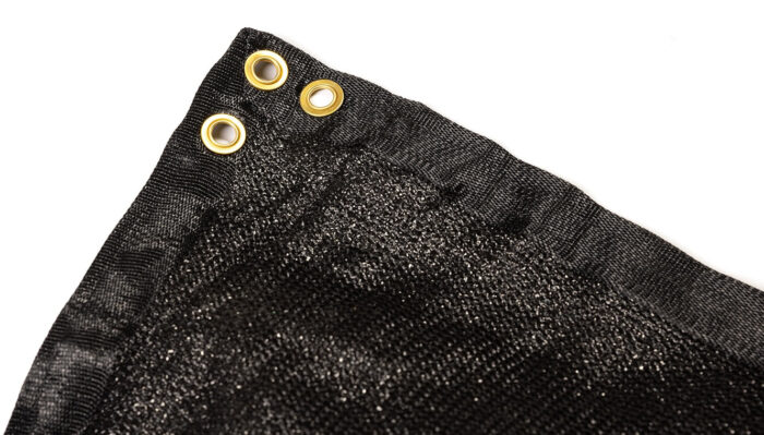 A close-up detail of a black temporary fence privacy screen, highlighting the durable woven fabric texture, double-stitched reinforced corner, and sturdy brass mounting grommets.